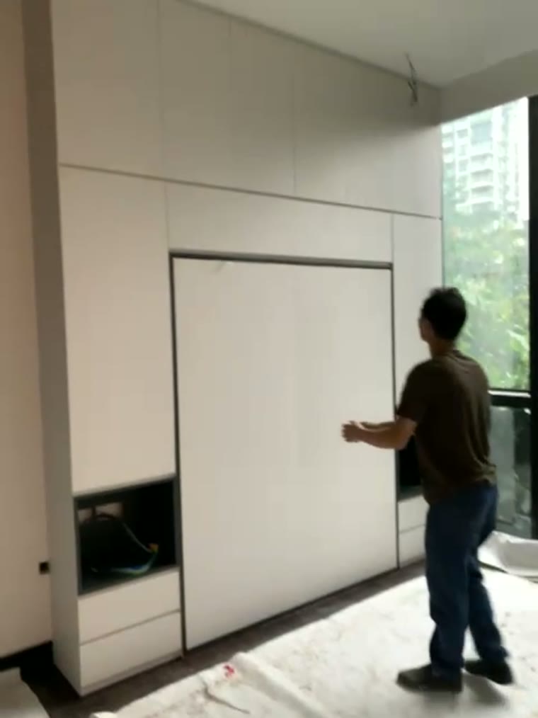 A completed white storage wall against floor-to-ceiling windows, the Murphy bed closed flush into the run.
