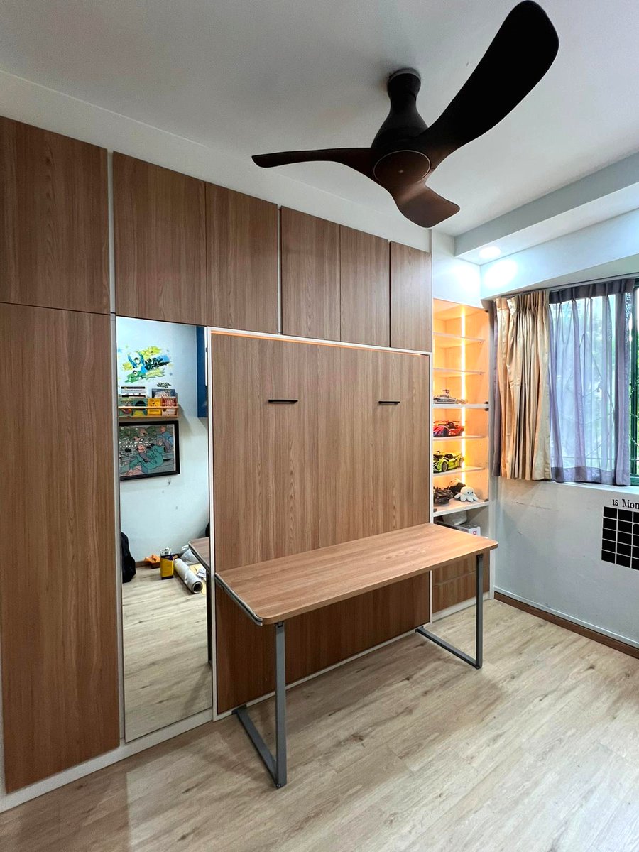 A completed Murphy bed wall in a Singapore bedroom, bed stowed, with the study desk out and lit display shelving alongside.