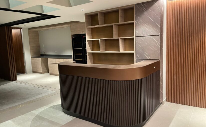 Curved fluted reception counter with brass-trimmed open shelving and stone cladding, Dunbar Walk landed home